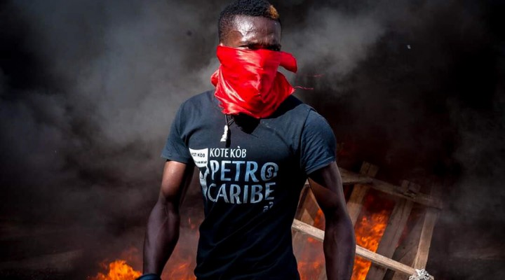 A young Haitian protestor wearing a Petro Caribe, a Venezuelan state-subsidized oil company, shirt, walks past a makeshift barricade during recent anti-government protests in Haiti